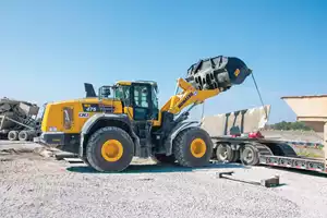 An operator lifts a metal plate with a Komatsu WA475-10 wheel loader during the setup of a batch plant.